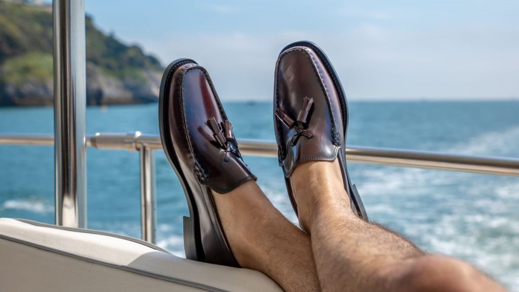 Close-up on male model's legs and feet propped up on boat side wearing tasselled loafers