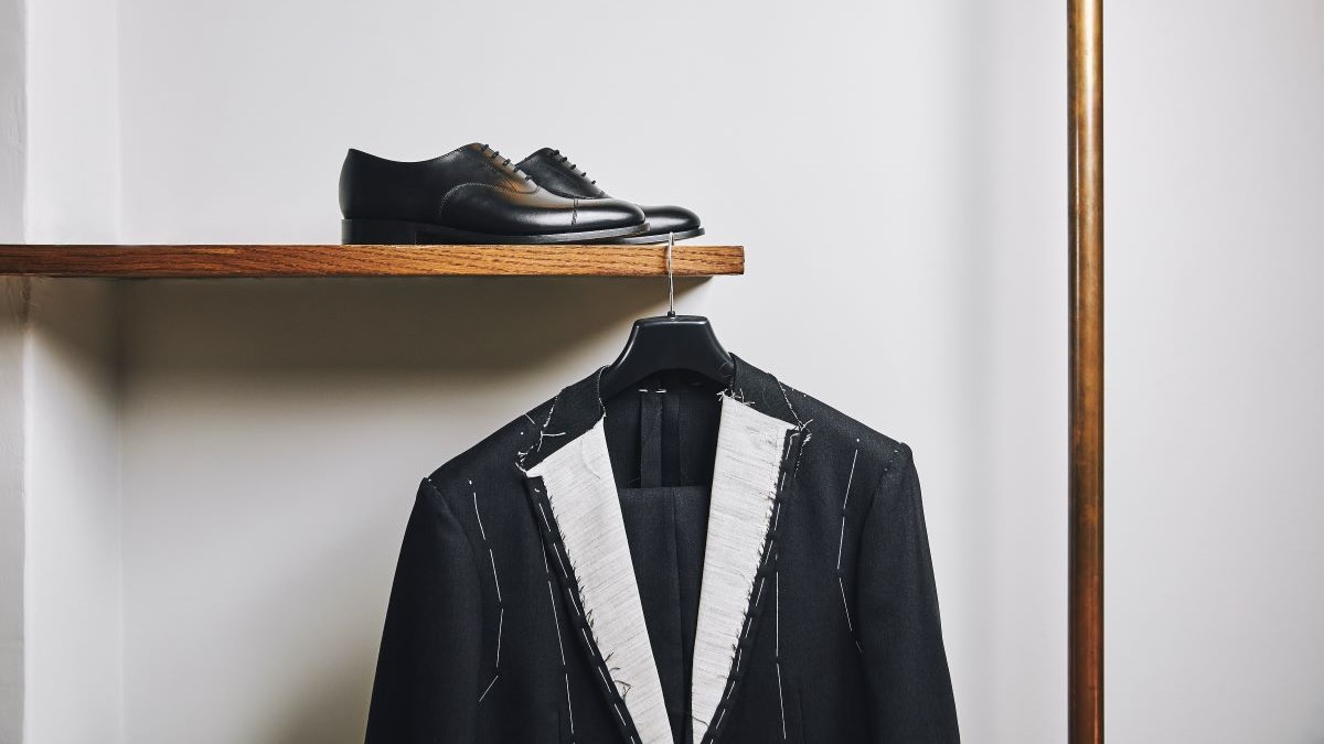 Black Oxford shoes on shelf from which a handmade suit jacket is hanging